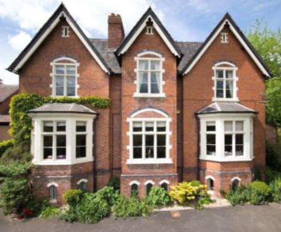 una casa de ladrillo con ventanas blancas y arbustos en Burleigh House B and B en Tenbury