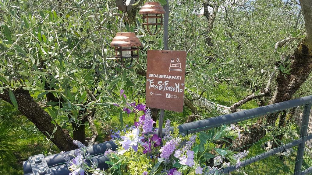 un cartello in un giardino con fiori e una recinzione di B&B ForseSiForseNo a Sulzano