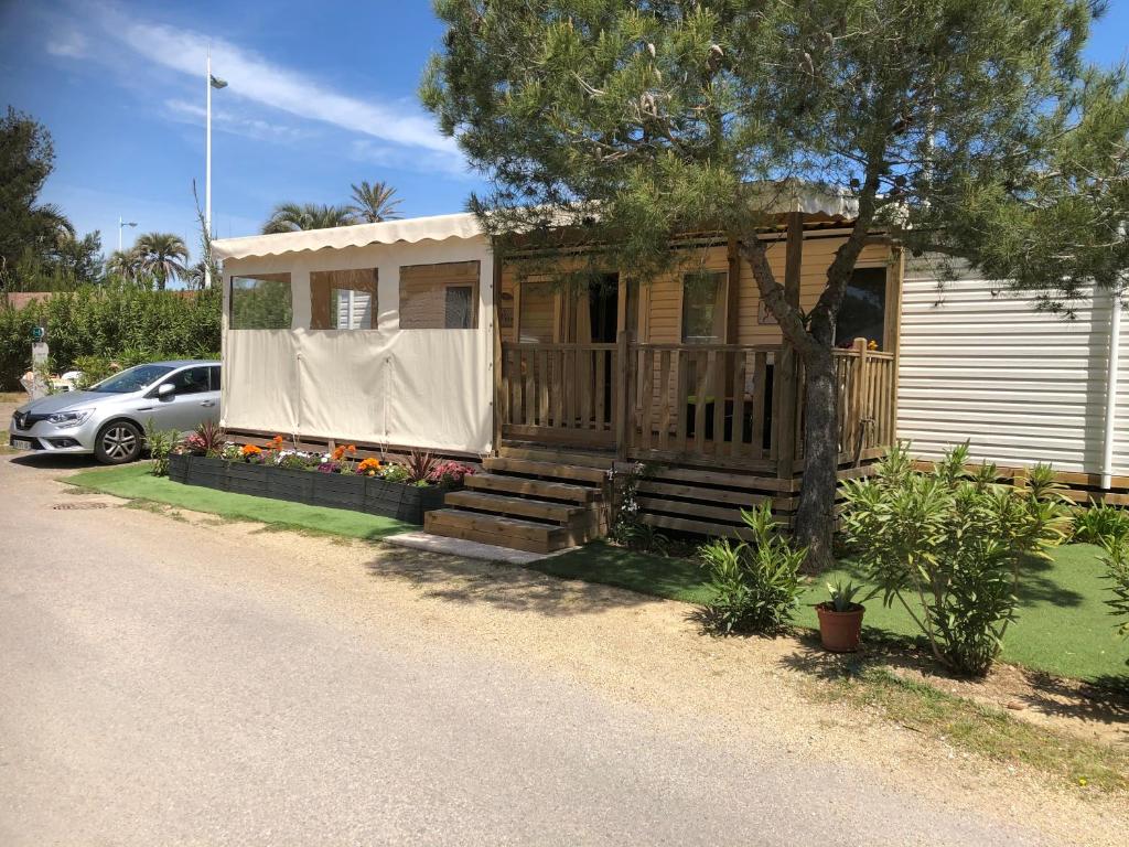 ein Haus mit einer Veranda und einem Auto daneben geparkt in der Unterkunft Mobilhome 2 Chambres 2 SDB in Canet-en-Roussillon