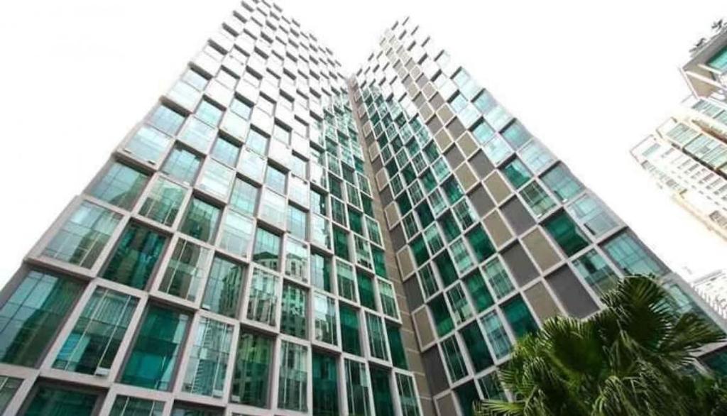 um edifício de vidro alto com palmeiras em frente em Soho Suites KLCC By iRent365 em Kuala Lumpur