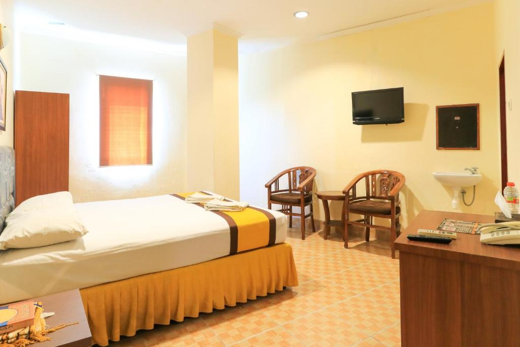 Al-Badar Hotel Syariah Makassar في ماكاسار: غرفة فندقية بسرير وطاولة وكراسي