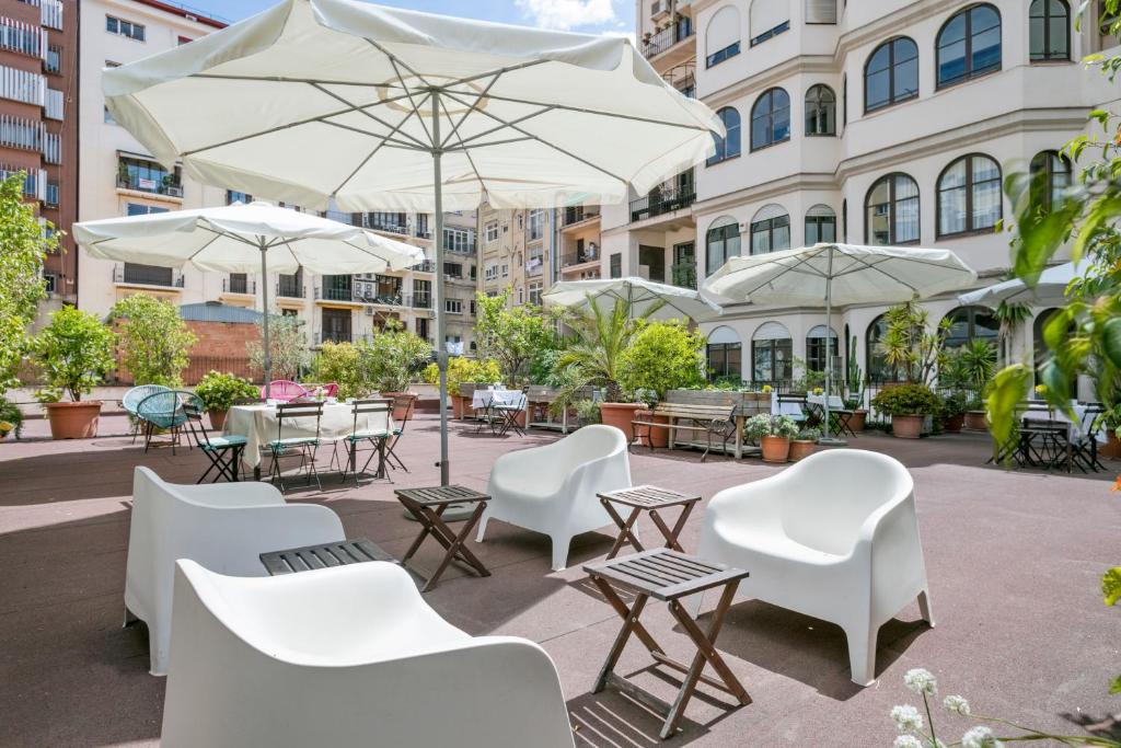 un patio con sedie bianche, tavoli e ombrelloni di Mihlton Barcelona Boutique B&B a Barcellona