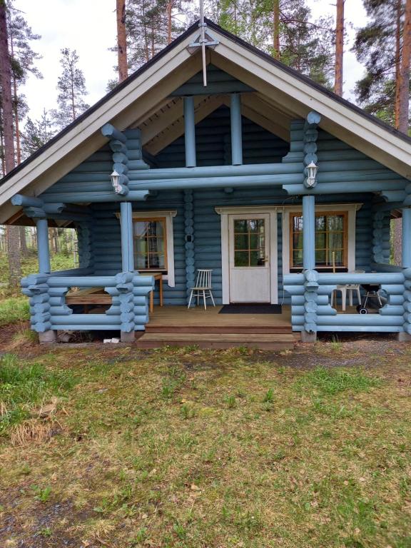 a blue cabin in the woods with a porch at Ellu in Kangasniemi