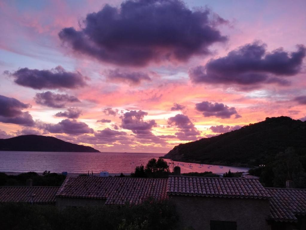 una puesta de sol sobre el agua con casas y una montaña en Demi villa à 150m de la plage avec vue sur mer en Appietto