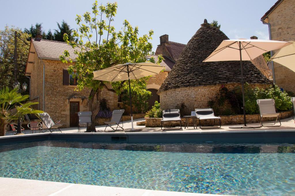 einen Pool mit Stühlen und Sonnenschirmen neben einem Haus in der Unterkunft Le Four à Pain, Gîte avec piscine et SPA proche Sarlat in Marquay