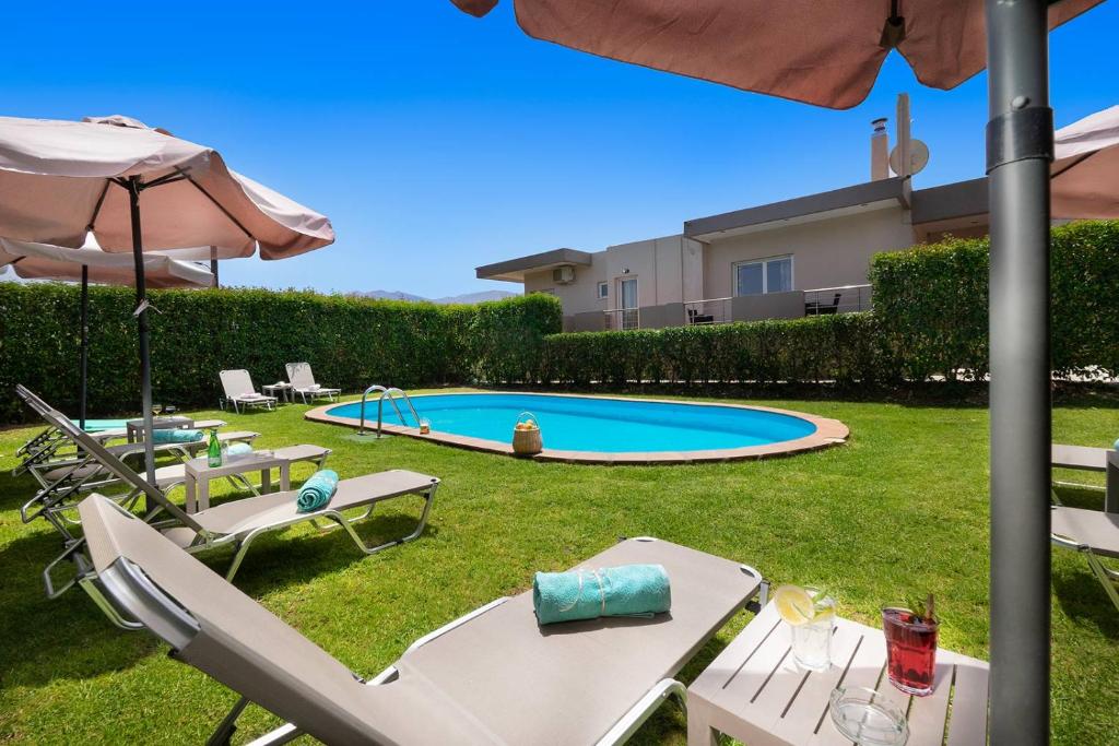 un patio trasero con piscina con sillas y sombrilla en Klironomos Art Villa, en Alikianós