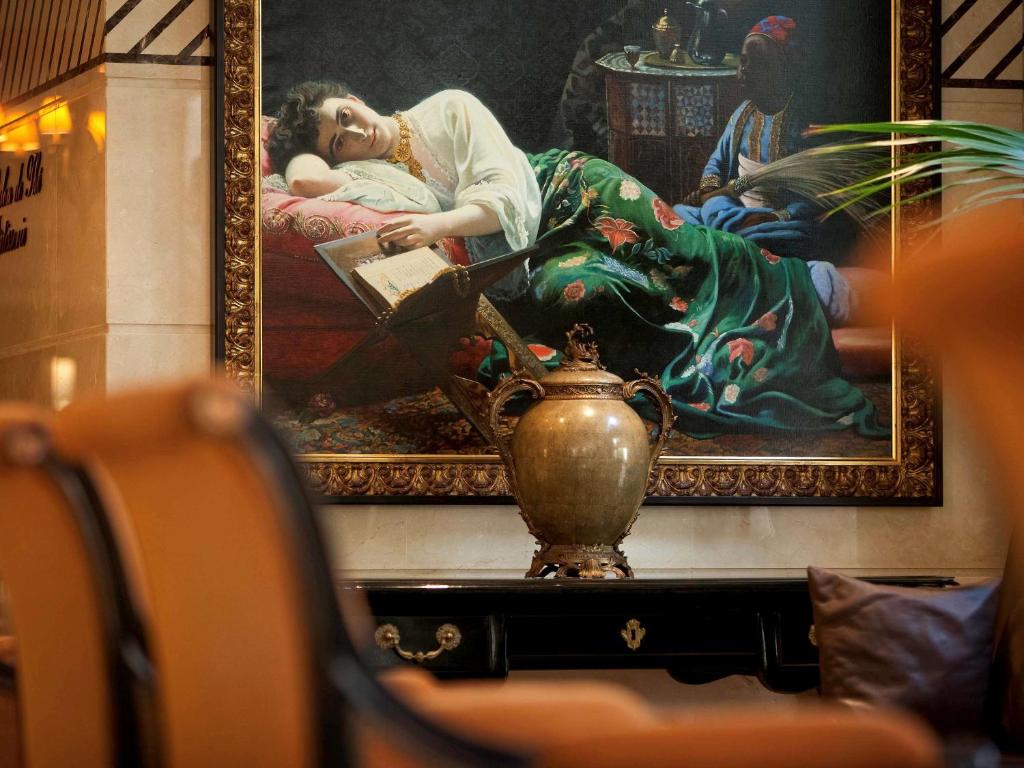 a painting of a woman sitting on a chair in front of a painting of at Royal Hotel Oran - MGallery Hotel Collection in Oran