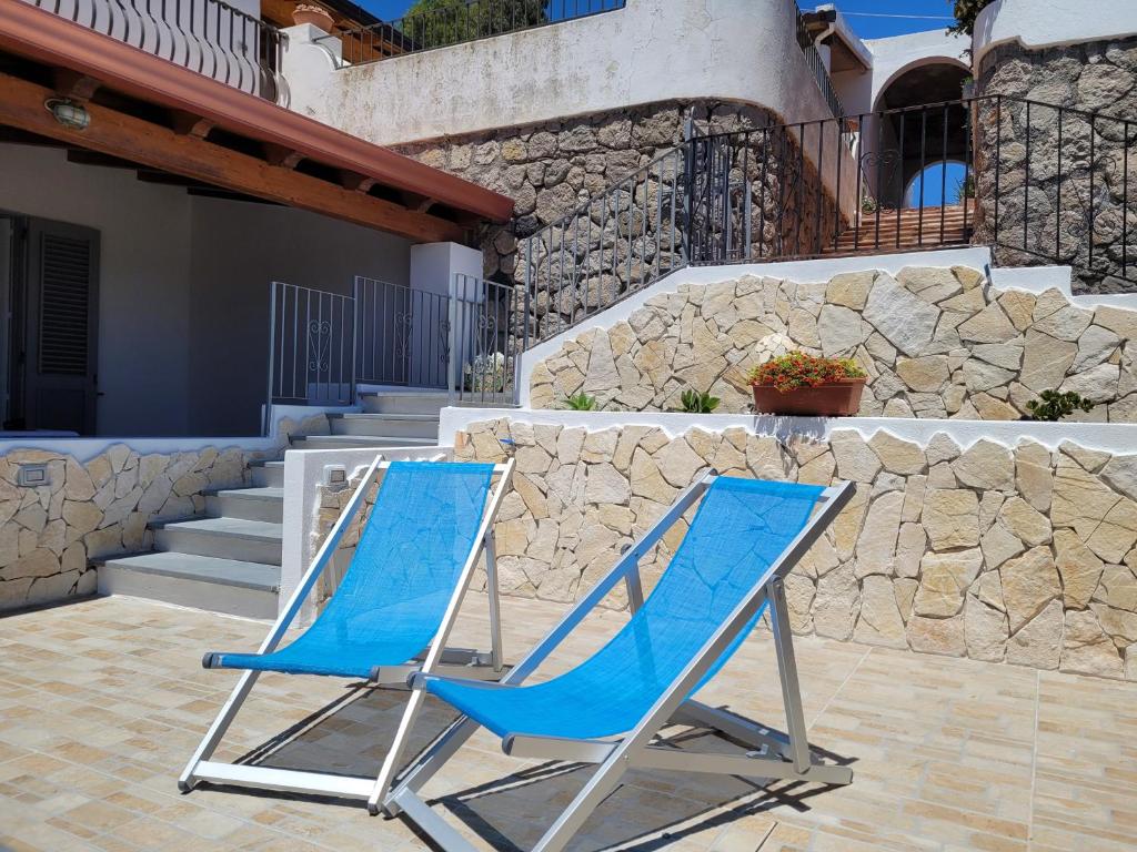 dwa niebieskie krzesła siedzące obok kamiennej ściany w obiekcie Casa Eolie relax w mieście Lipari
