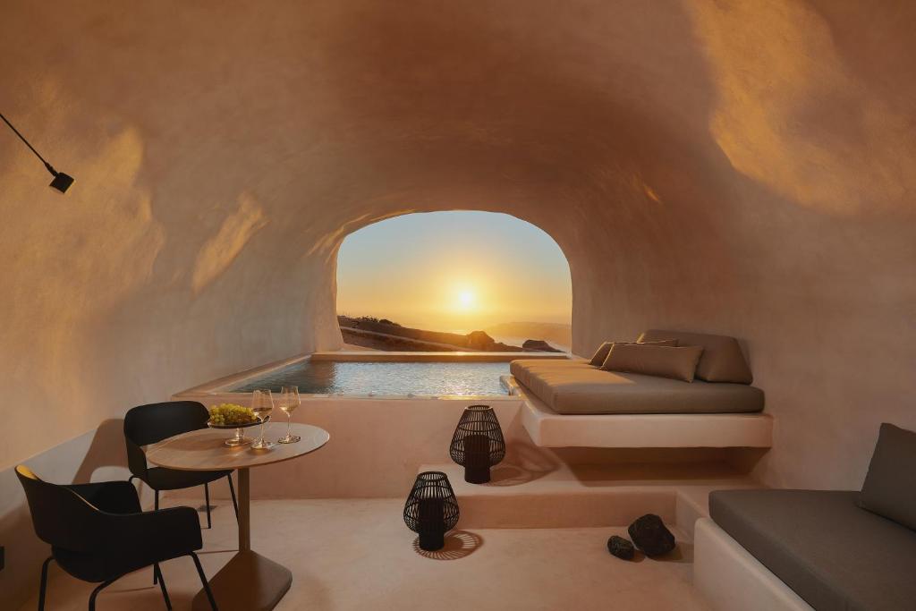 a room with a bed and a table and a sunset at Divine Cave Experience in Imerovigli