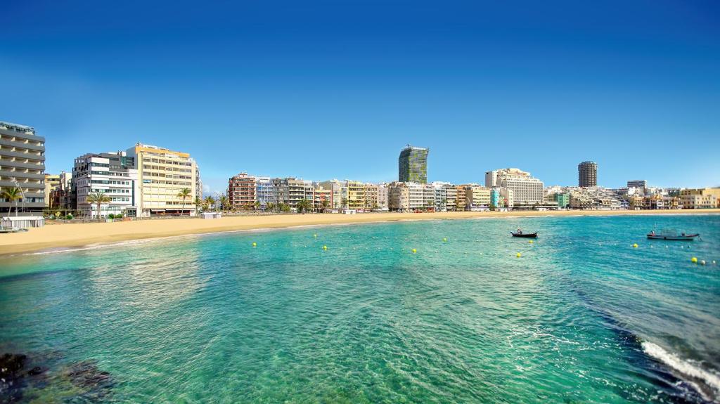 uma praia com dois barcos na água e uma cidade em First line new apartment in Las Canteras em Las Palmas de Gran Canárias