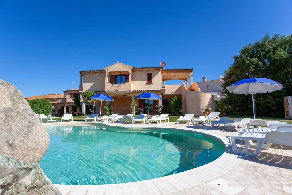 a swimming pool with chairs and umbrellas in front of a house at Il Viandante in San Teodoro
