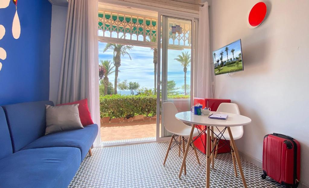 a living room with a blue couch and a table and a window at Sunrise Studio Miro, vistas jardín y mar in Miami Platja