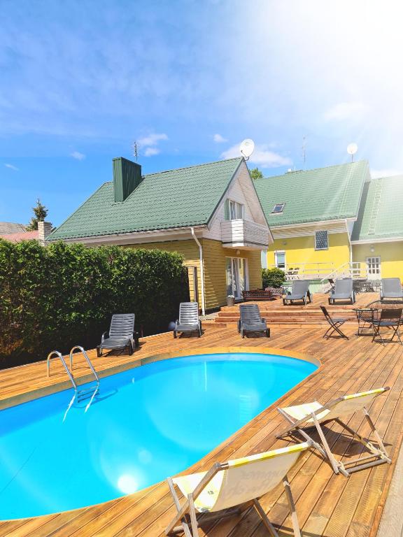 a swimming pool on a deck with chairs and a house at SAULES SVECIU NAMAI in Palanga