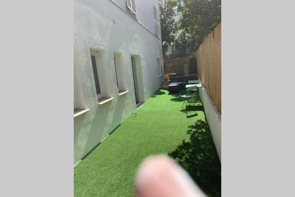 une petite cour avec de l'herbe verte sur le côté d'un bâtiment dans l'établissement Appartement neuf 4-6 personnes en bord de Mer, à Nice