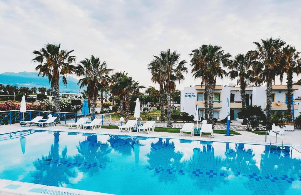 a large swimming pool with chairs and palm trees at 1-Bedroom Kos Olympia Apartment at Lambi Beach in Kos Town