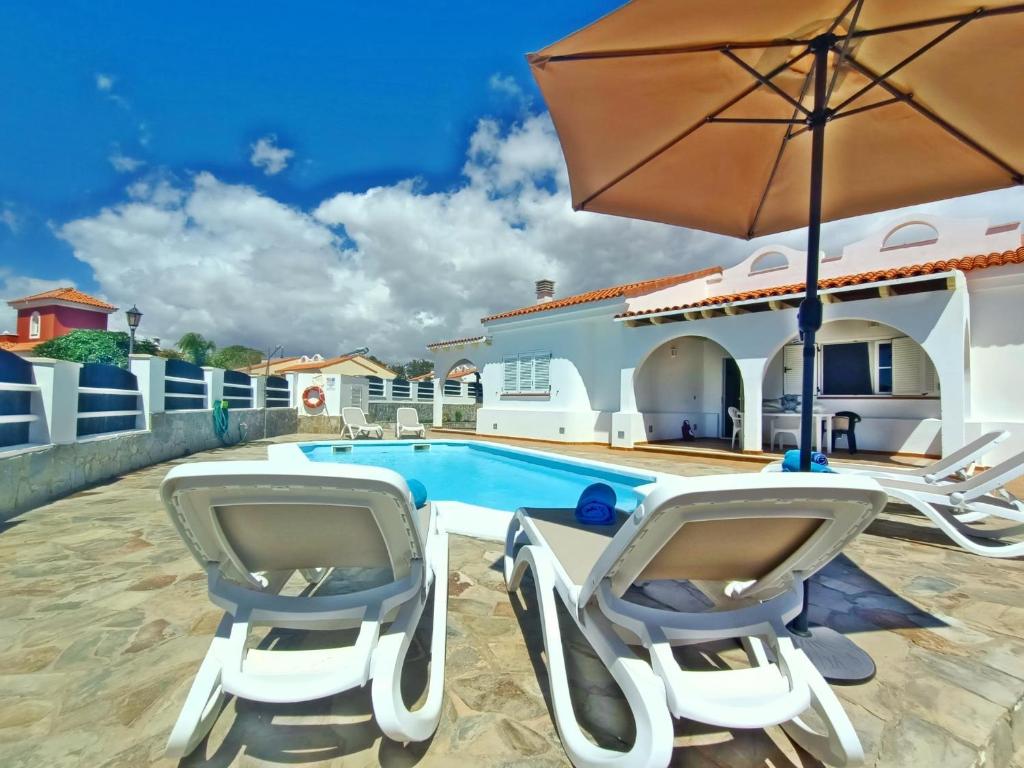 een villa met een zwembad, 2 stoelen en een parasol bij Vv JARA in Caleta De Fuste