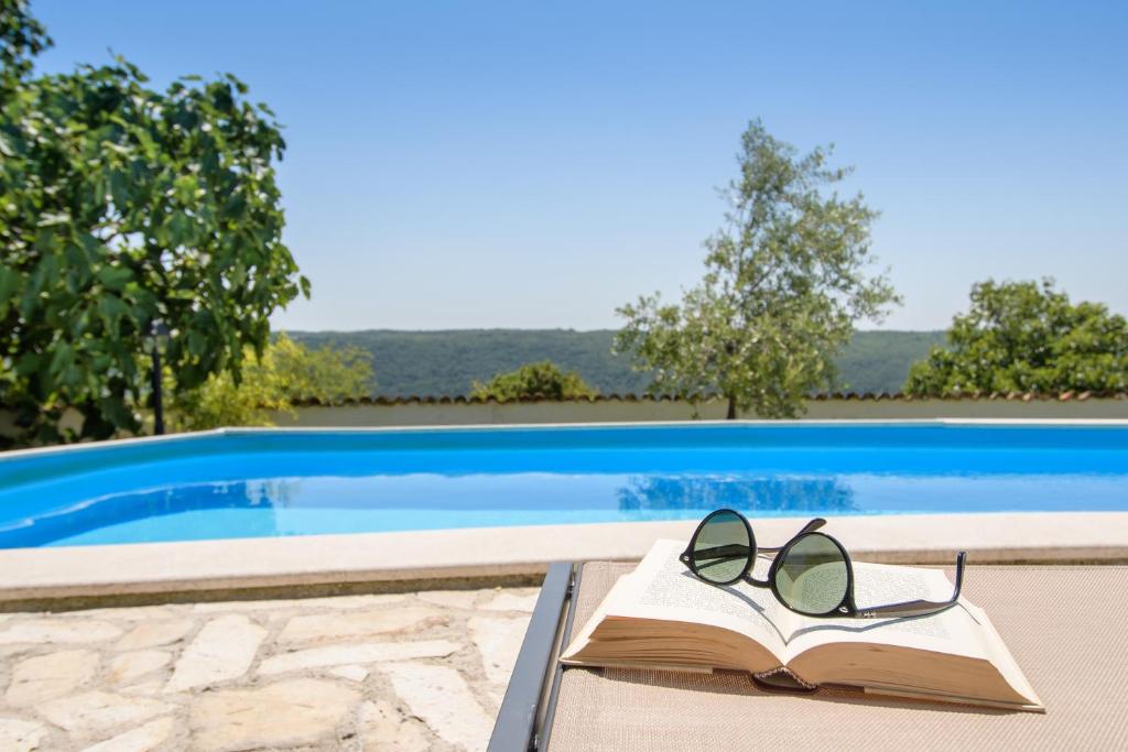 un libro y gafas en una mesa junto a una piscina en Villa C'est la vie, en Buje