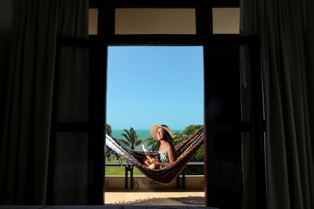 una donna seduta su un'amaca sul balcone di Dolce Vita Guest House a Lagoinha