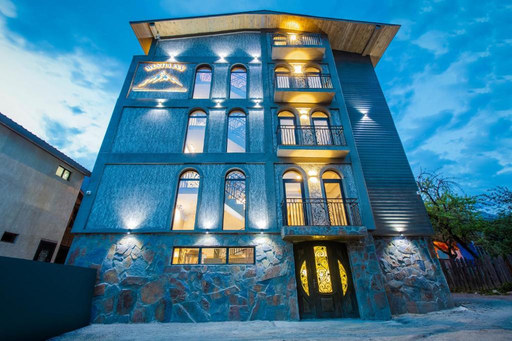 Un bâtiment bleu avec des lumières allumées la nuit dans l'établissement Hotel Mestia Inn, à Mestia