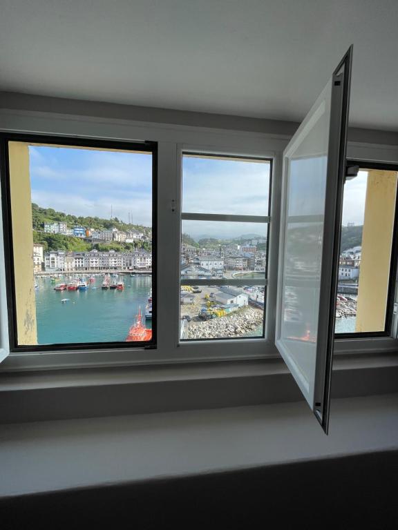 a room with three windows with a view of a harbor at Atico El Puerto in Luarca
