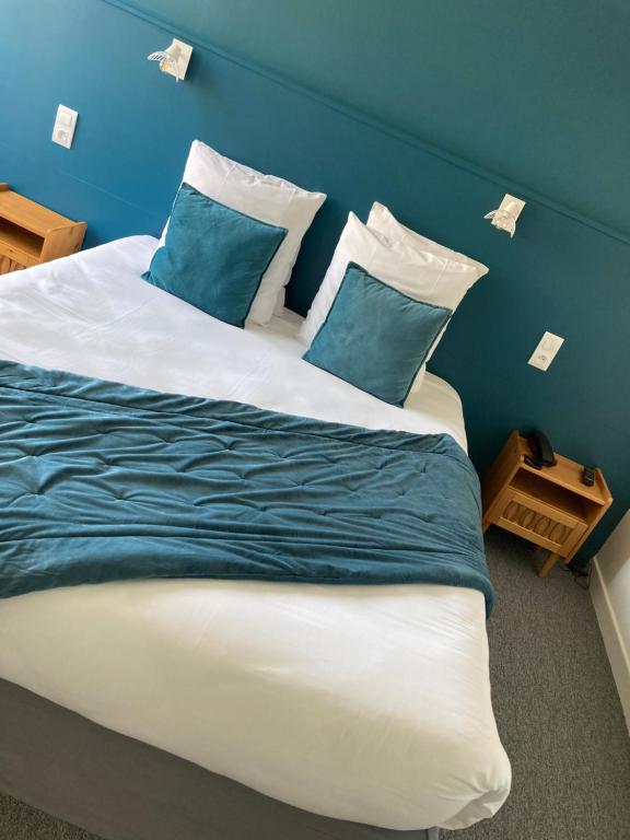 a large bed with blue and white sheets and pillows at Hôtel de la Mer in Pléneuf-Val-André