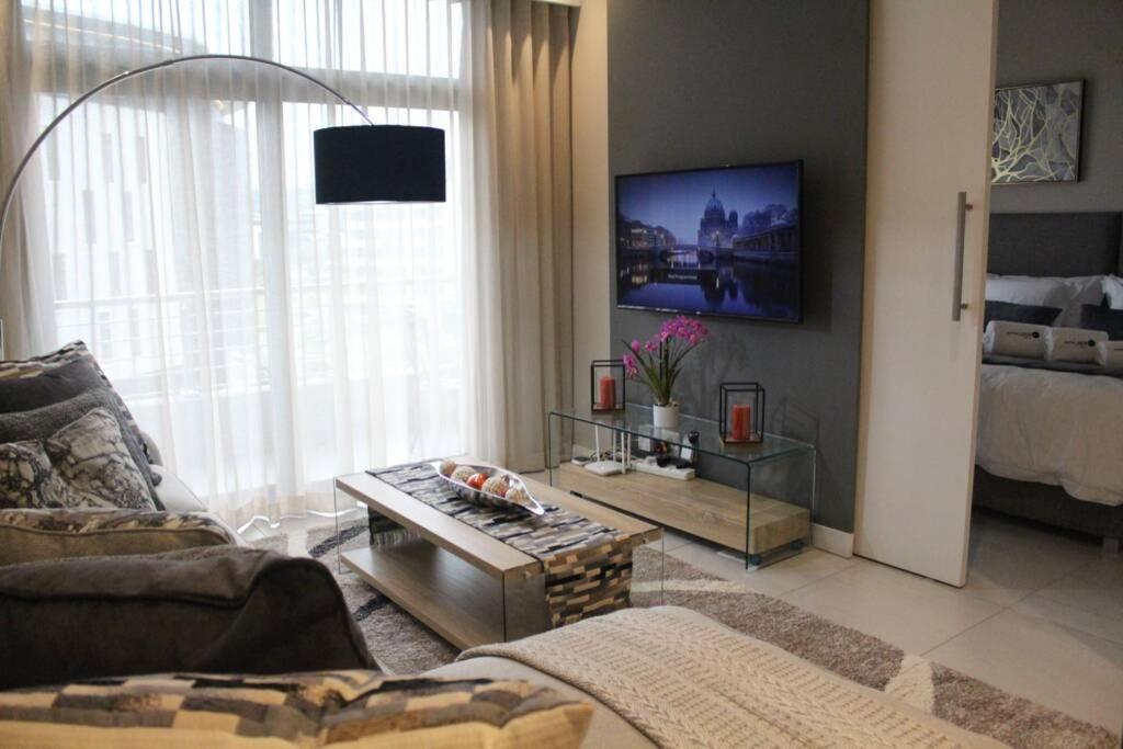 a living room with a couch and a table at Furnished, 1-bedroom, luxury apartment in Menlyn Maine in Pretoria