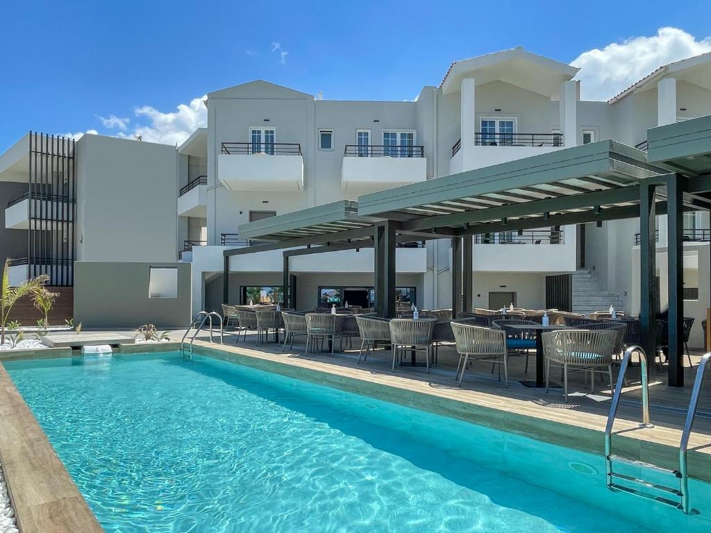 a swimming pool with tables and chairs next to a building at Mare Blue Suites in Georgioupolis