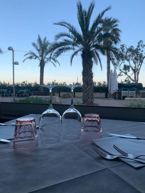 a table with two wine glasses on a table with palm trees at Hotel Svizzera in Arma di Taggia