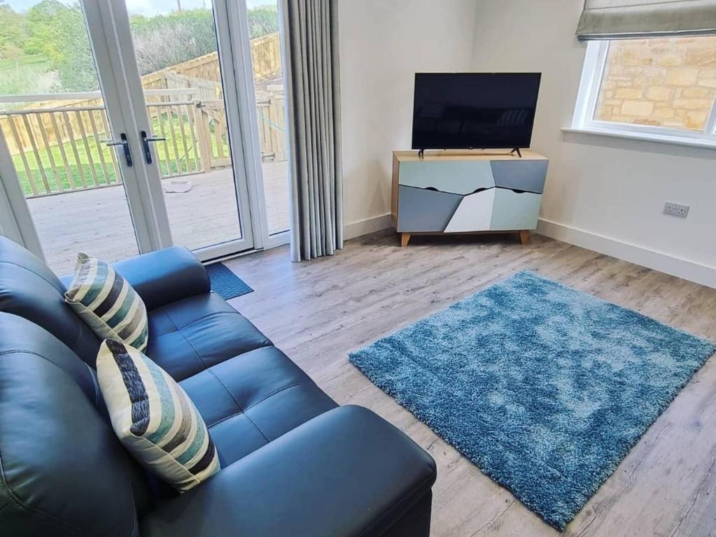 a living room with a leather couch and a television at Beech Cottage in Rothbury