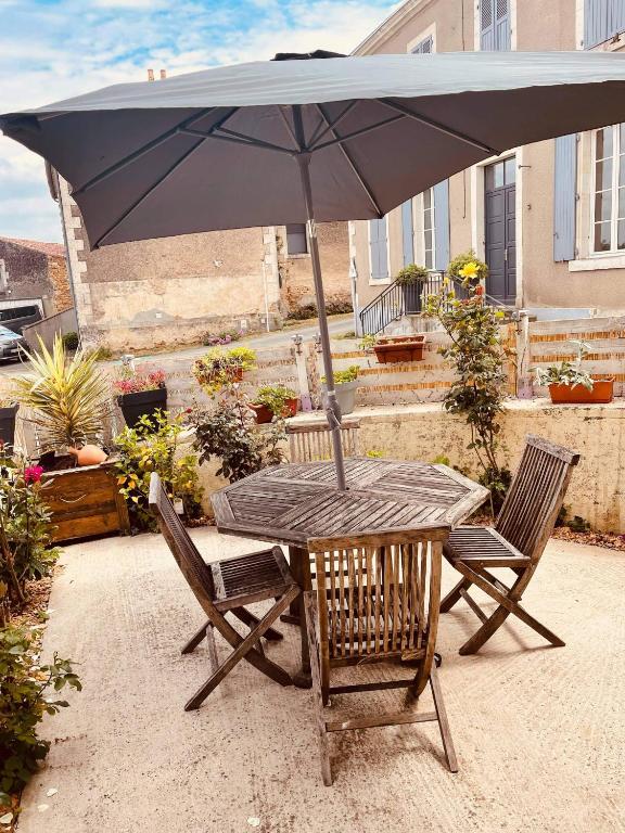 une table en bois avec un parasol et deux chaises dans l'établissement charmante maison de village renovée, à Bazoges-en-Pareds