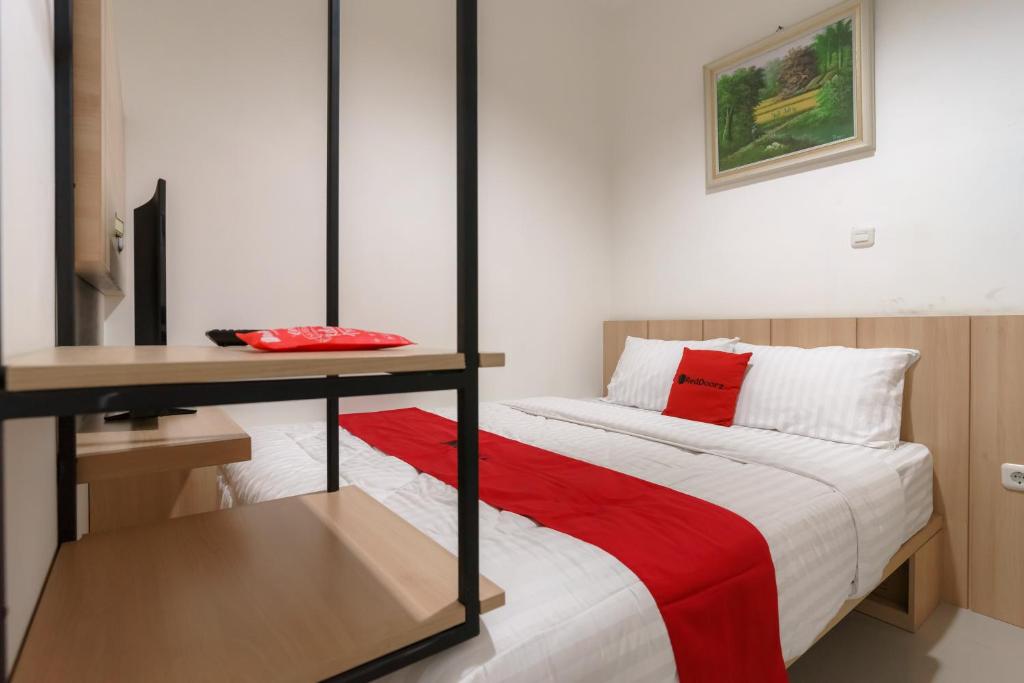 um quarto com uma cama, uma secretária e um cobertor vermelho em RedDoorz near Seasons City Mall 3 em Jakarta
