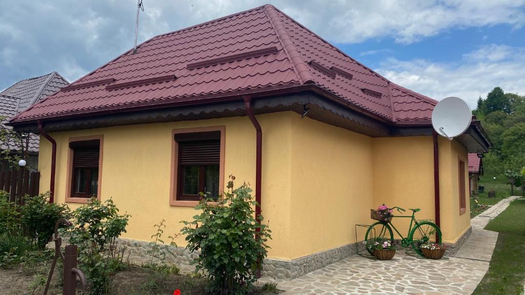 una casa amarilla con techo púrpura y bicicleta en Casa de vacanta - Ograda cu flori en Almaş