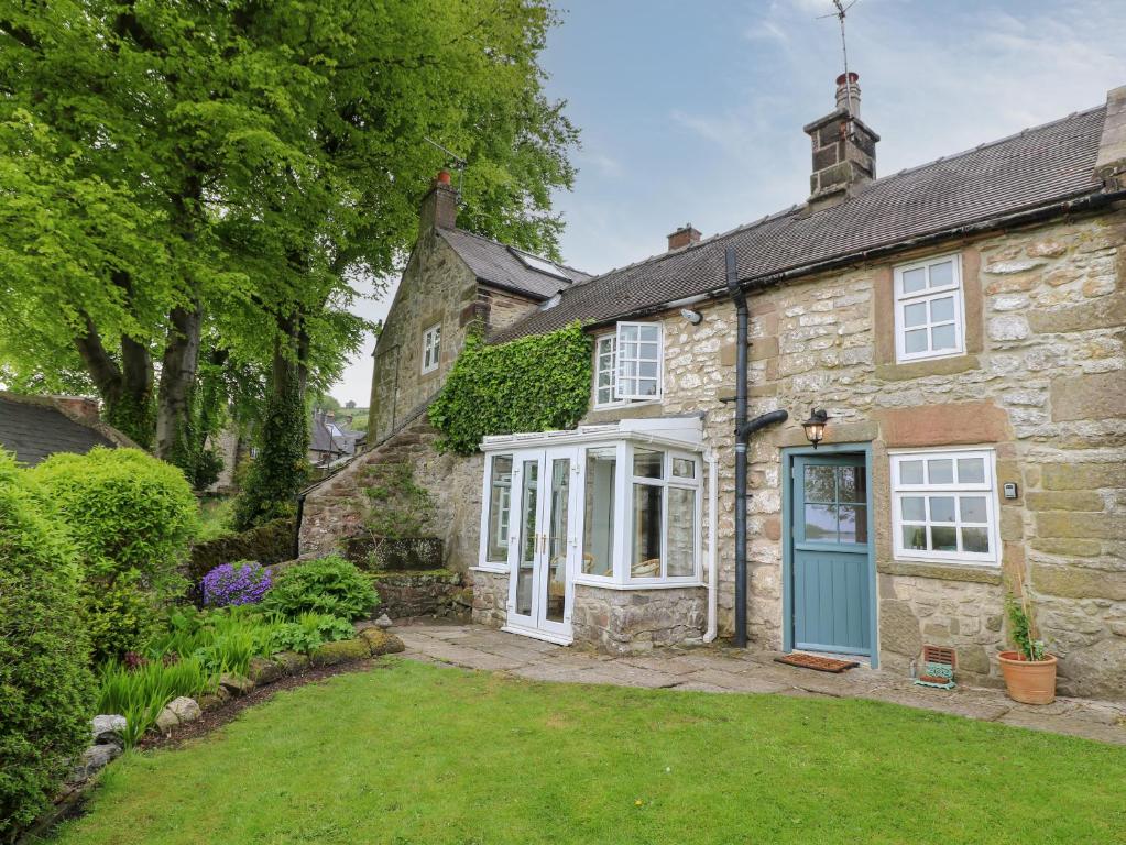 an old stone house with a blue door and a yard at Ivy Cottage in Matlock