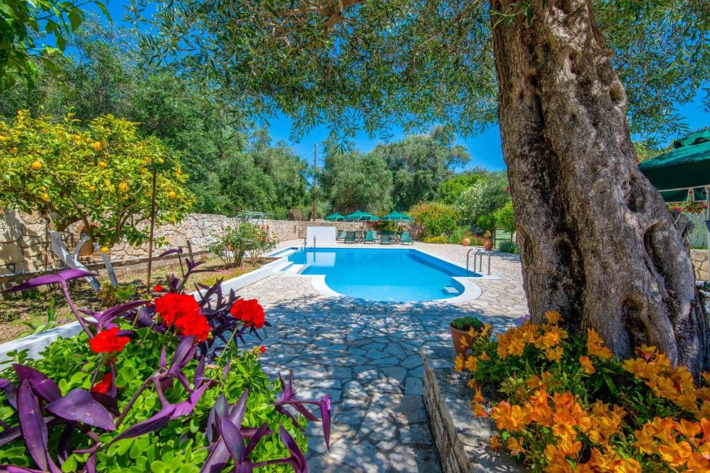 a pool in a garden with flowers and a tree at LIvadi Studios with Pool in Lákka