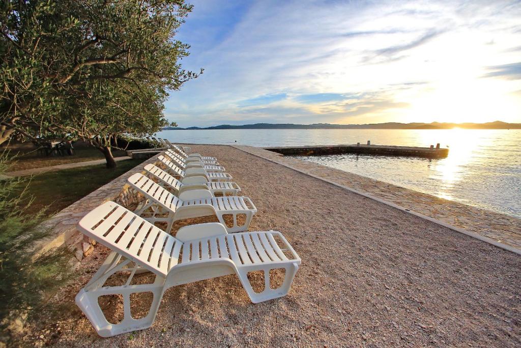 rząd białych krzeseł ustawionych na plaży w obiekcie APARTMANI GORDANA w Bibinje