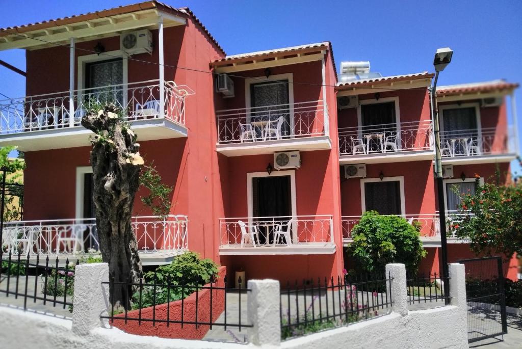 a red house with white balconies on a street at Rio Grande Rooms in Benitses