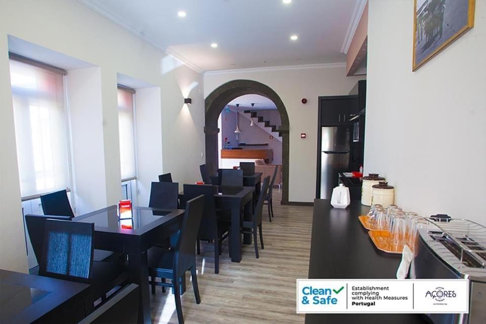 un restaurant avec des tables et des chaises noires et une cuisine dans l'établissement D. Irene Hostel, à Lajes
