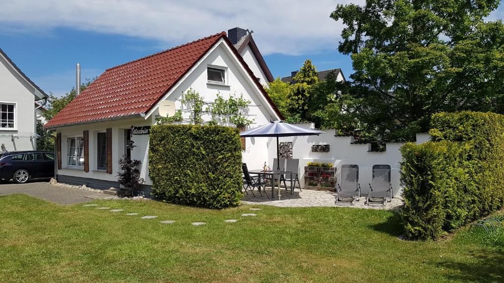 a white house with a table and an umbrella at Ferienhaus Ostseebrise Usedom im Grünen familienfreundlich ruhig Parkplatz Terrasse Kamin in Ostseebad Karlshagen