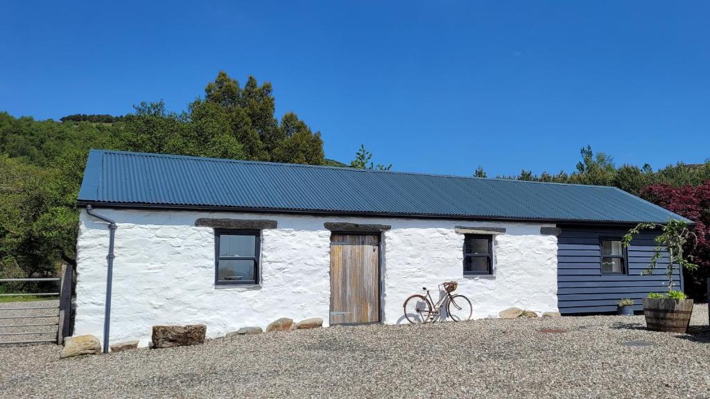 ein weißes Cottage mit einem Fahrrad, das davor geparkt ist in der Unterkunft Loch Lomond Blair Byre in Rowardennan