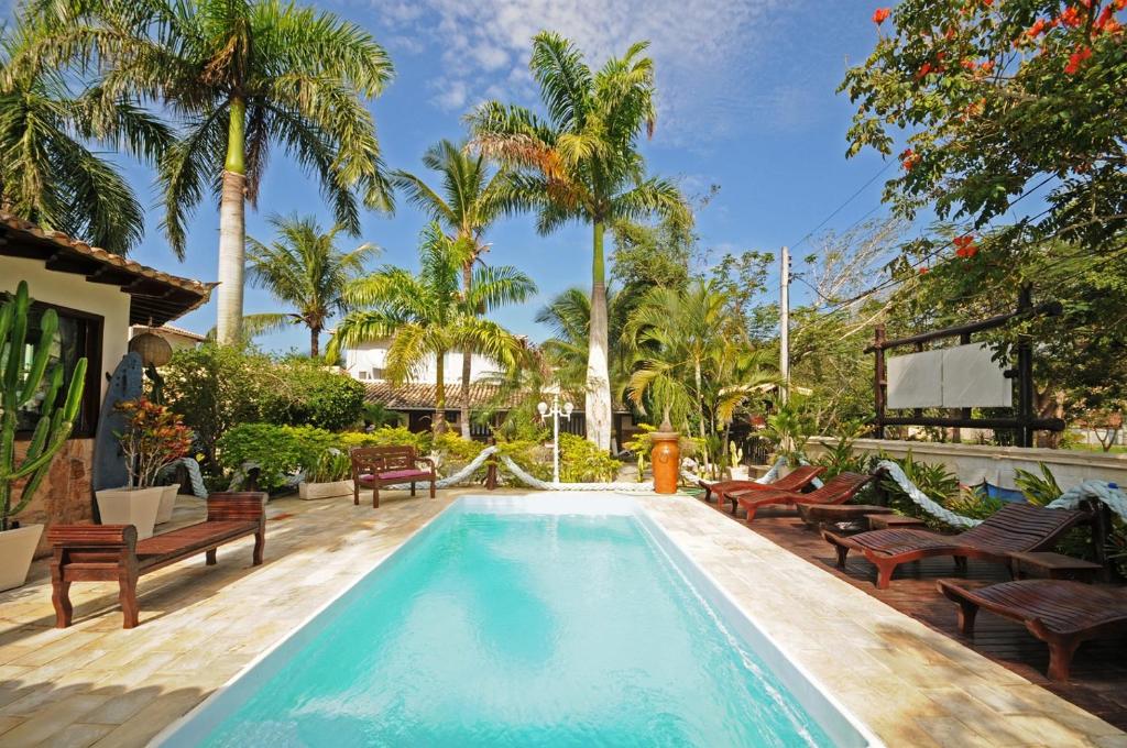 a swimming pool with benches and palm trees at Mar e Terra Concept Pousada in Búzios