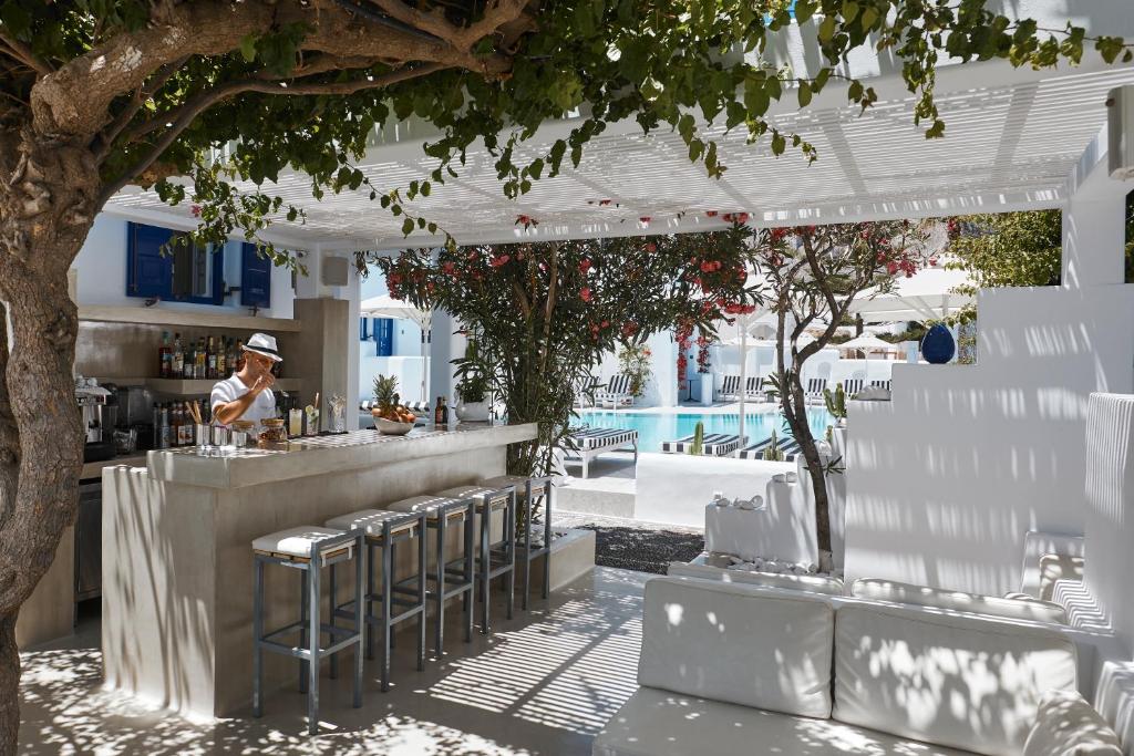 a bar with stools and a man standing at a counter at Kouros Village Hotel - Adults Only in Perissa