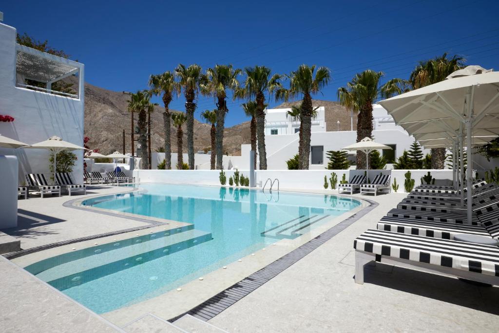 - une piscine bordée de chaises et de palmiers dans l'établissement Kouros Village Hotel - Adults Only, à Perissa