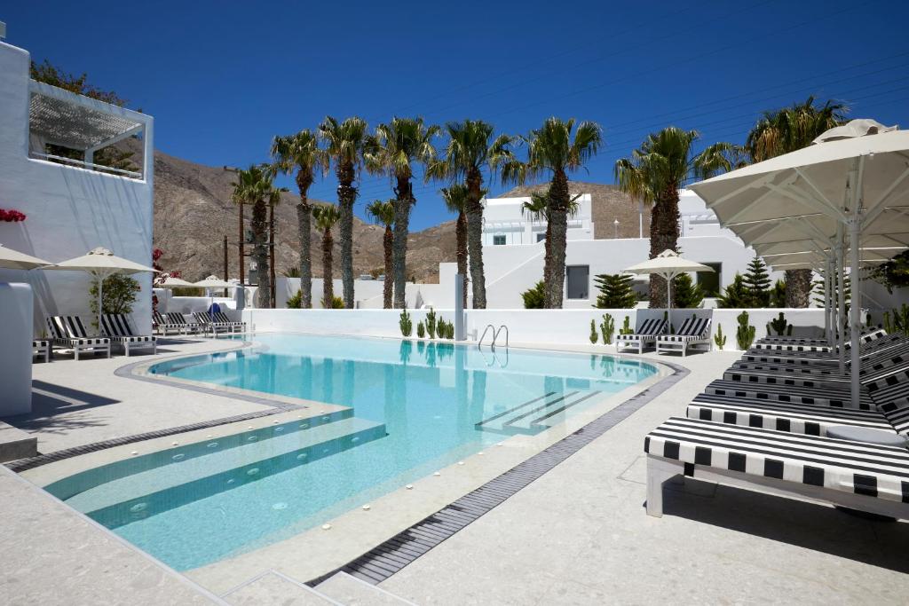 a swimming pool with chairs and palm trees at Kouros Village Hotel - Adults Only in Perissa