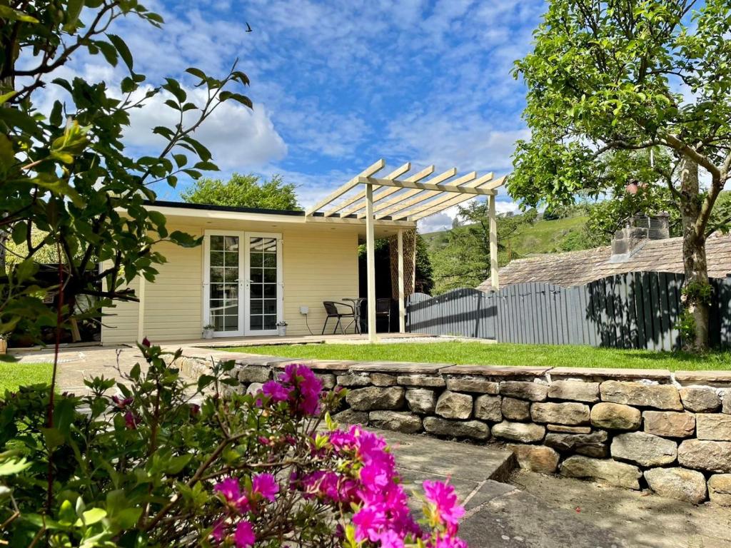 a small white house with a stone wall and flowers at Apple tree hut, in a private garden in Skipton