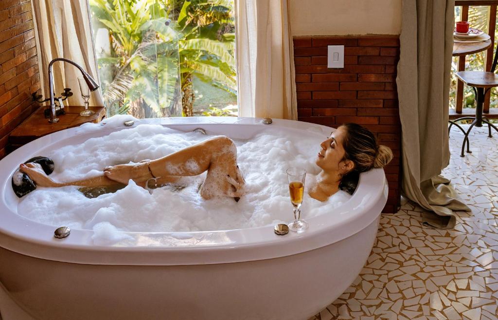 Una donna sdraiata in una vasca da bagno con un bicchiere di vino di Chales Sol Paraty a Parati