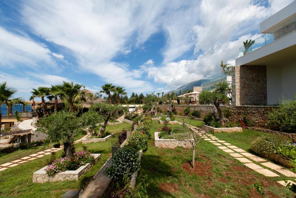 a garden in front of a building with trees and bushes at Empire Beach Resort ADULTS ONLY in Dhërmi