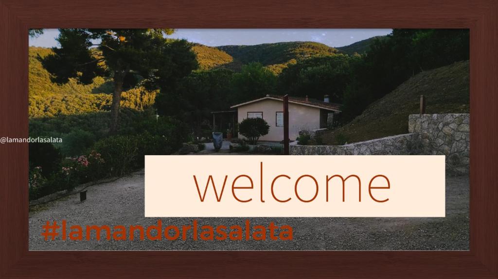 un cartello che dice benvenuto con una casa sullo sfondo di La Mandorla Salata a Capoliveri
