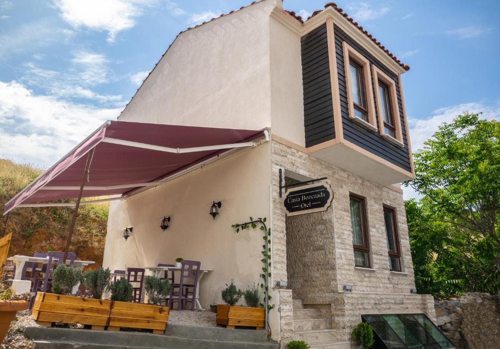 a small white building with a purple umbrella and benches at Mare Casia Bozcaada Otel in Bozcaada
