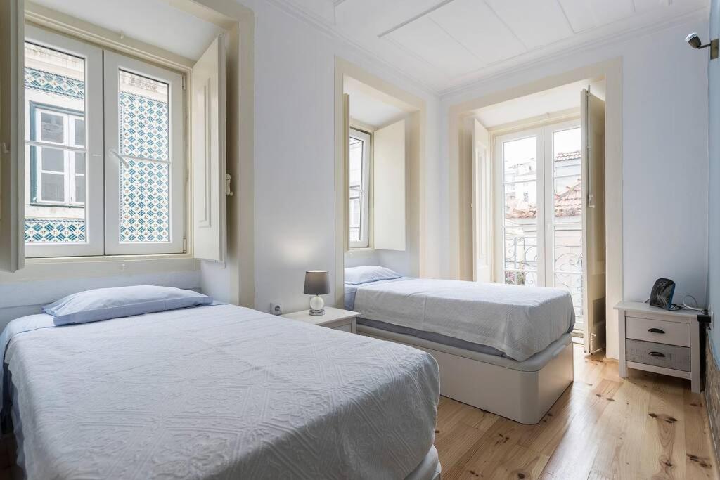 two beds in a white room with two windows at Flat do Chiado 02 in Lisbon