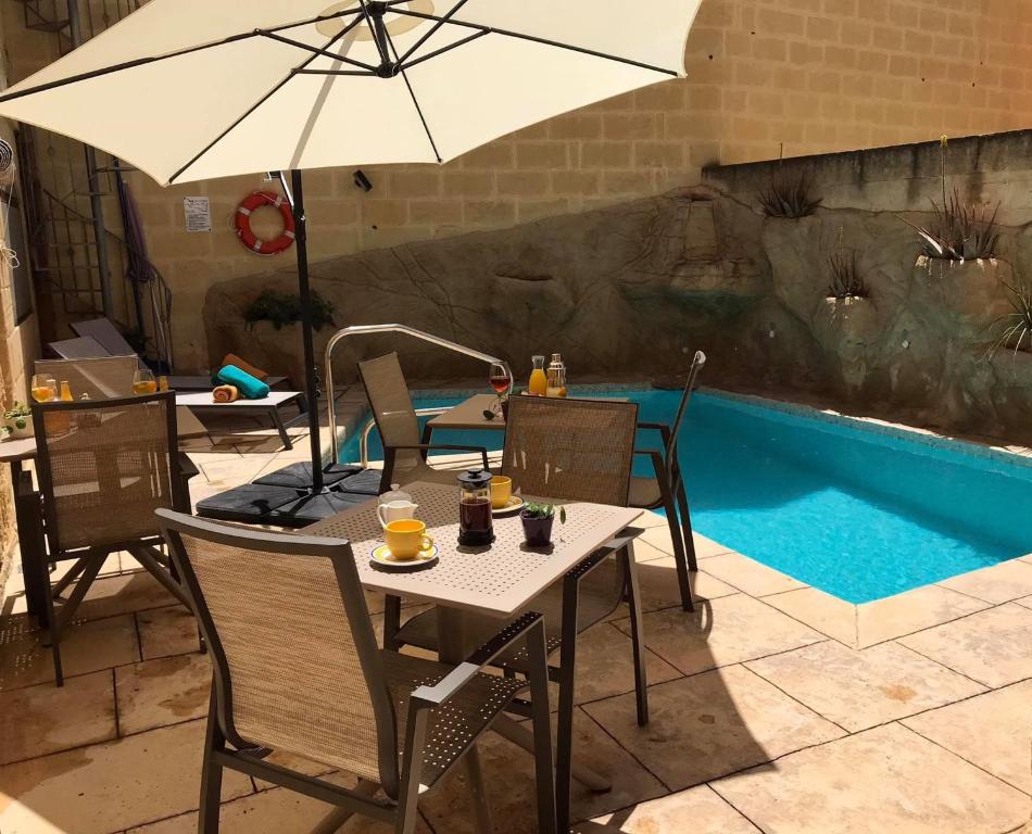 stół i krzesła z parasolem przy basenie w obiekcie Ta Marie Merhba w mieście Żebbuġ